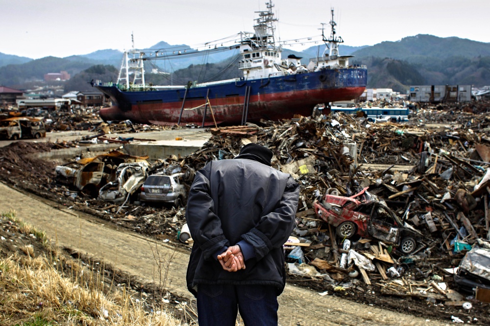 Пожилой японец смотрит с холма на разрушенный цунами город Исиномаки. 2011 г.